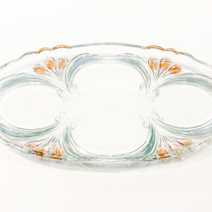 May include: A clear glass serving tray with an oval shape and a decorative design of stylised flowers with orange accents.