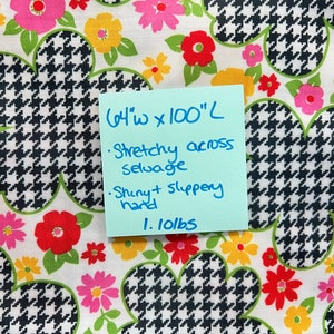 May include: Black and white houndstooth fabric with a floral print in shades of pink, red, yellow, and green. The fabric is 64 inches wide and 100 inches long. It is stretchy across the selvage and has a shiny, slippery hand. The fabric weighs 1.10 lbs.