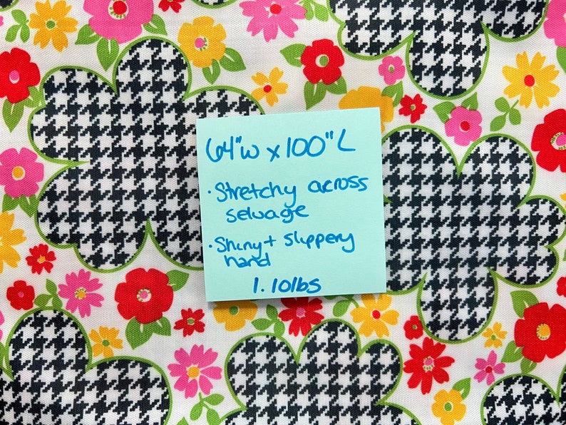 May include: Black and white houndstooth fabric with a floral print in shades of pink, red, yellow, and green. The fabric is 64 inches wide and 100 inches long. It is stretchy across the selvage and has a shiny, slippery hand. The fabric weighs 1.10 lbs.