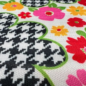 May include: White fabric with a black and white houndstooth pattern, green leaves, and colorful flowers in shades of red, pink, yellow, and orange.