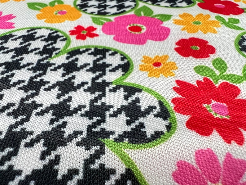 May include: White fabric with a black and white houndstooth pattern, green leaves, and colorful flowers in shades of red, pink, yellow, and orange.