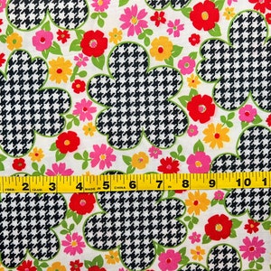 May include: White fabric with a repeating pattern of black and white houndstooth flowers and colorful floral accents. A yellow measuring tape is placed at the bottom of the image.