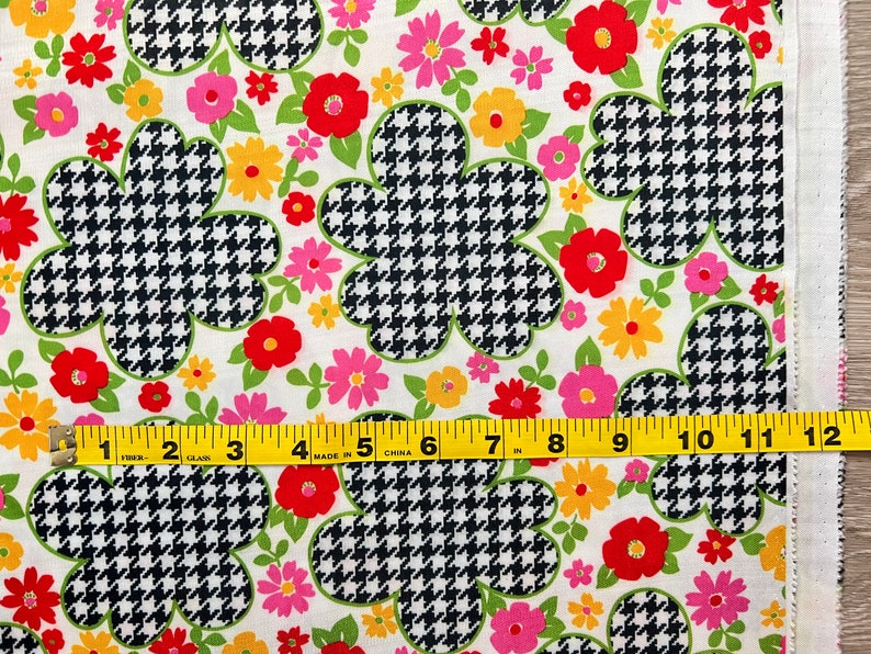 May include: White fabric with a repeating pattern of black and white houndstooth flowers and colorful floral accents. A yellow measuring tape is placed at the bottom of the image.