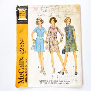 Könnte beinhalten: Vintage McCall's 2256 Schnittmuster für Damenkleider und Schal. Das Schnittmuster enthält drei Kleiderdesigns mit Knopfleisten und Taillen mit Gürtel. Das Cover zeigt Illustrationen der Kleider in verschiedenen Farben und Mustern.