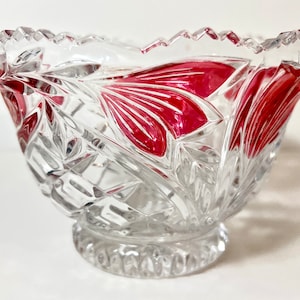 May include: A clear glass bowl with a cut glass design and a red rim. The bowl has a scalloped edge and a small, round base.