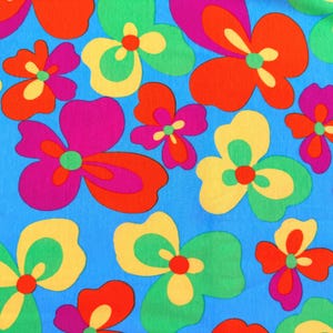 May include: A fabric featuring a vibrant floral pattern with stylized flowers in shades of bright orange, magenta, yellow, and green set against a solid sky blue background. The repeating design consists of rounded, organic petal shapes.