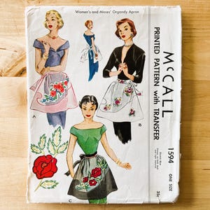 May include: A vintage McCall 1594 sewing pattern envelope for an organdy apron. The white paper cover features illustrations of three apron styles with floral embroidery designs, including red roses and green leaves, alongside the text McCall 1594.