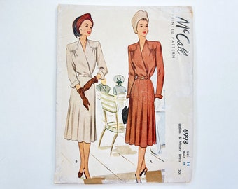 May include: Vintage McCall's sewing pattern for a dress, size 14, bust 34. The pattern features two women wearing dresses with different colors and styles. The text on the pattern reads "McCall's Printed Pattern 6998 Ladies' & Misses' Dress 50c".