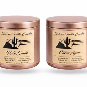 Può includere: Due barattoli di candele color rame con etichette che recitano "Sedona Vortex Candles". Uno è etichettato "Palo Santo" e l'altro "Citrus Agave". Ogni etichetta presenta un paesaggio desertico con un cactus. Le candele sono in cera di soia.