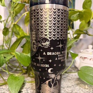 Puede incluir: Vaso de acero inoxidable negro con un dise&ntilde;o de drag&oacute;n plateado y el texto "A dragon without a rider is a rider without a dragon. Or die as riders." Incluye una pajita y una tapa negra.