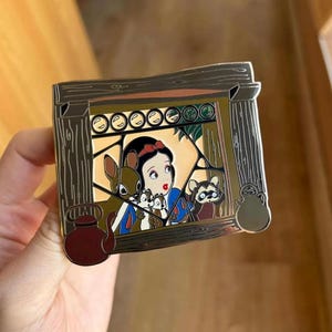 May include: A rectangular enamel pin featuring Snow White and forest animals framed by a wooden window design. The pin has a brown and silver color scheme, with a detailed illustration of the Disney princess and her woodland friends.
