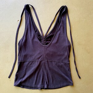 May include: A dark purple vest top with a V-neck and spaghetti straps that tie at the shoulders. The back features crisscrossing straps and a ruched detail. The top is made of a soft, stretchy fabric.