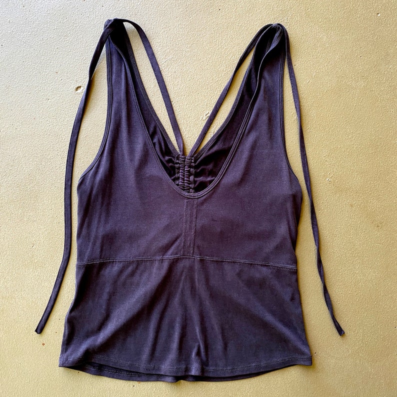 May include: A dark purple vest top with a V-neck and spaghetti straps that tie at the shoulders. The back features crisscrossing straps and a ruched detail. The top is made of a soft, stretchy fabric.
