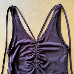May include: A dark purple vest top with a ruched front and spaghetti straps. The straps cross at the back and tie at the shoulders. The top has a V-neck and a fitted shape.