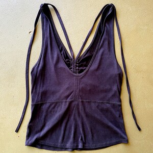 May include: Dark purple tank top with a V-neck and spaghetti straps that tie at the shoulders. The back features crisscross straps and a ruched detail. The top is made of a soft, stretchy material.