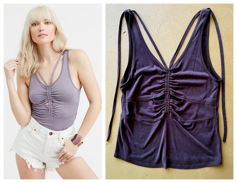 May include: A lilac-coloured tank top with a ruched front and a keyhole detail. The top has thin straps that tie at the shoulders. The fabric appears soft and has a slight sheen. The style is casual and suitable for warm weather.