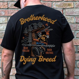 May include: Black t-shirt with a graphic of a skeleton working on a high voltage power line. The text on the shirt reads "Brotherhood of a Blue Collar High Voltage Dying Breed".