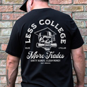 May include: Black t-shirt with a white graphic of a skull wearing a graduation cap and holding a diploma. The text "Less College More Trades" is printed below the skull. The text "Dirty Hands, Clean Money" is printed below the text "More Trades". The text "Est. MMXXII" is printed below the text "Dirty Hands, Clean Money".