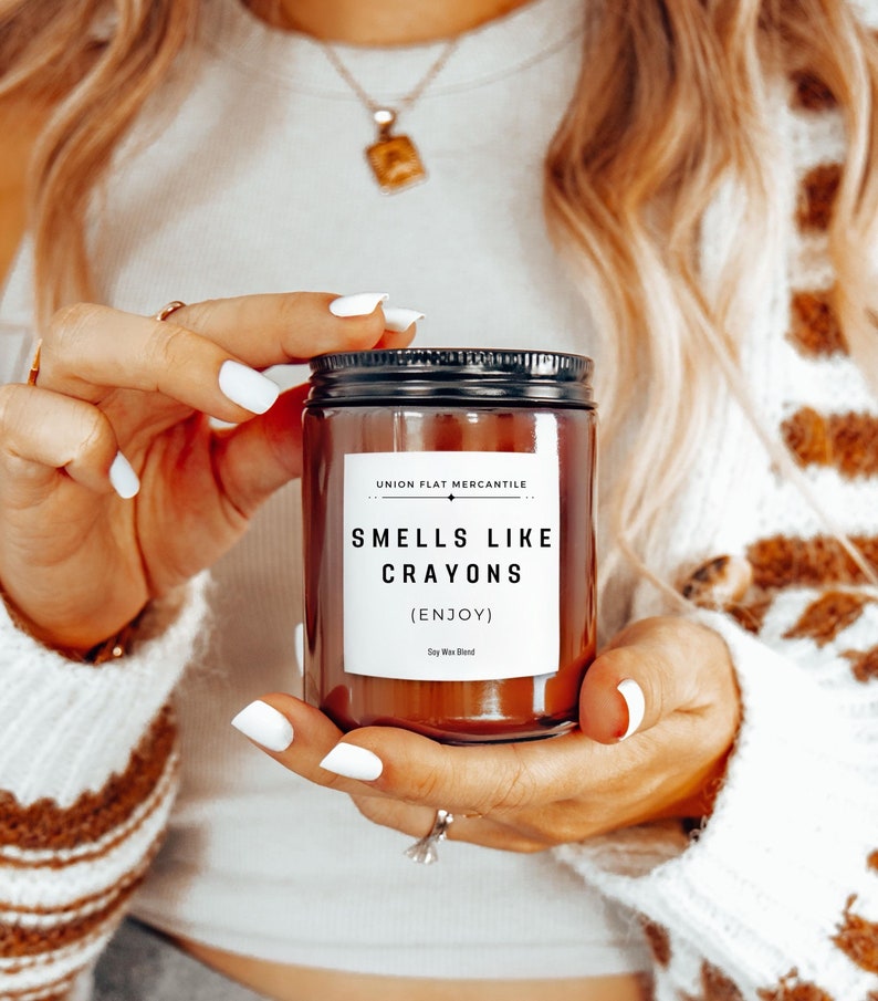 May include: A brown glass candle jar with a black lid and a white label that reads "UNION FLAT MERCANTILE" and "SMELLS LIKE CRAYONS (ENJOY) Soy Wax Blend".