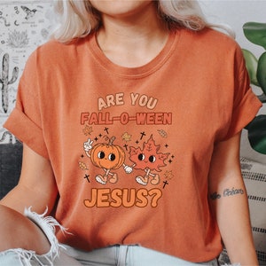 May include: A burnt orange t-shirt with the text "Are you Fall-O-Ween Jesus?" in white. A cartoon pumpkin and leaf with faces are holding hands.