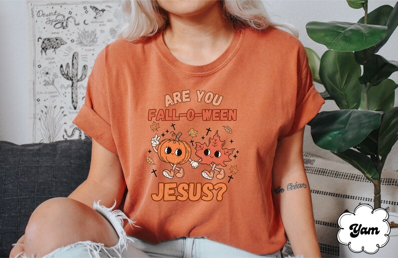 May include: A burnt orange t-shirt with the text "Are you Fall-O-Ween Jesus?" in white. A cartoon pumpkin and leaf with faces are holding hands.