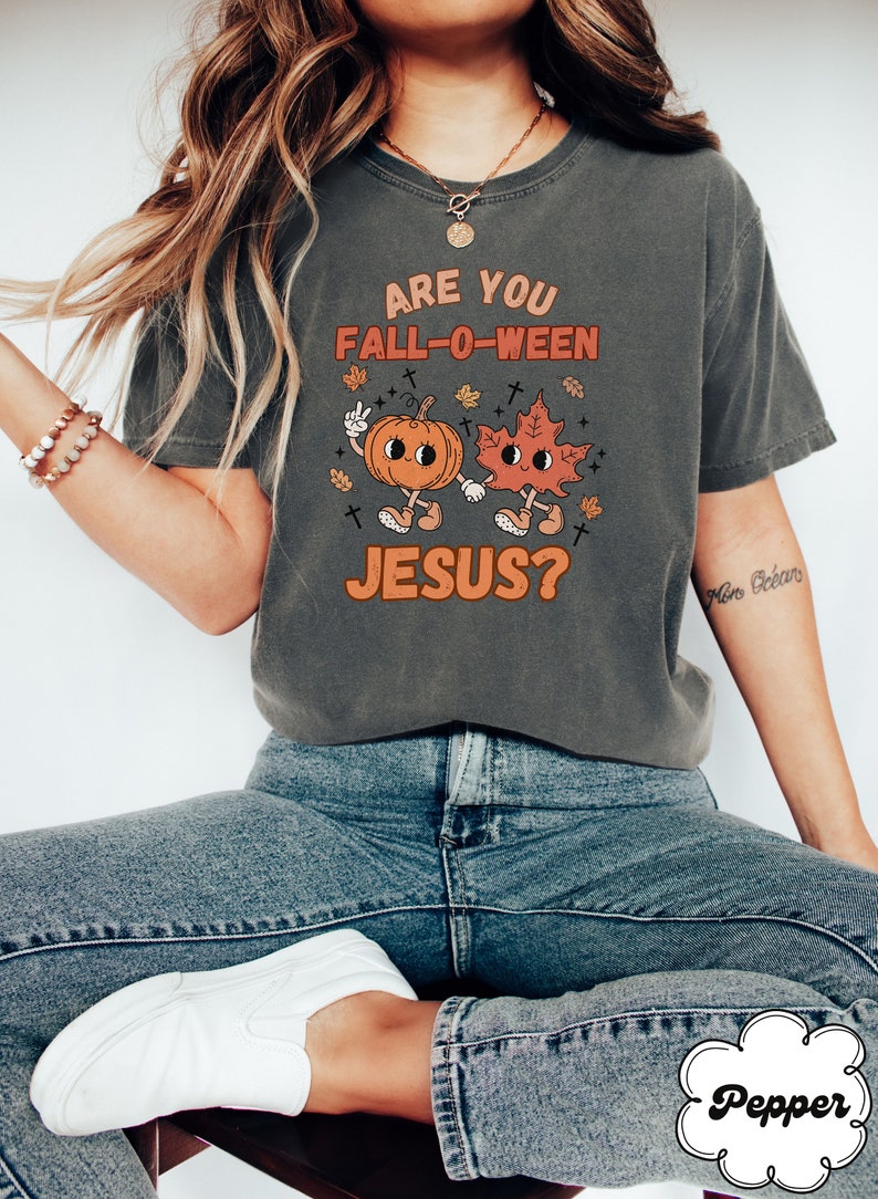 May include: A grey t-shirt with a graphic of a pumpkin and a leaf holding hands. The text on the shirt reads "Are you Fall-O-Ween Jesus?"