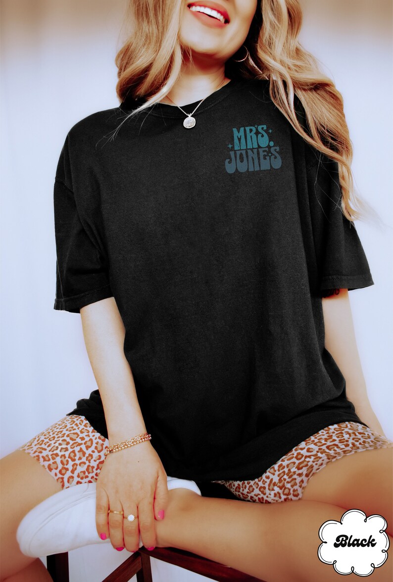 Może przedstawiać: Czarny T-shirt z napisem "MRS. JONES" w retro czcionce.