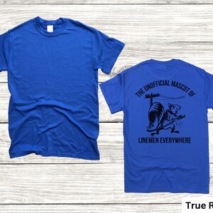 May include: True Royal blue t-shirt. The front of the shirt is plain. The back of the shirt features a black graphic of a rat with the text "THE UNOFFICIAL MASCOT OF LINEMEN EVERYWHERE".