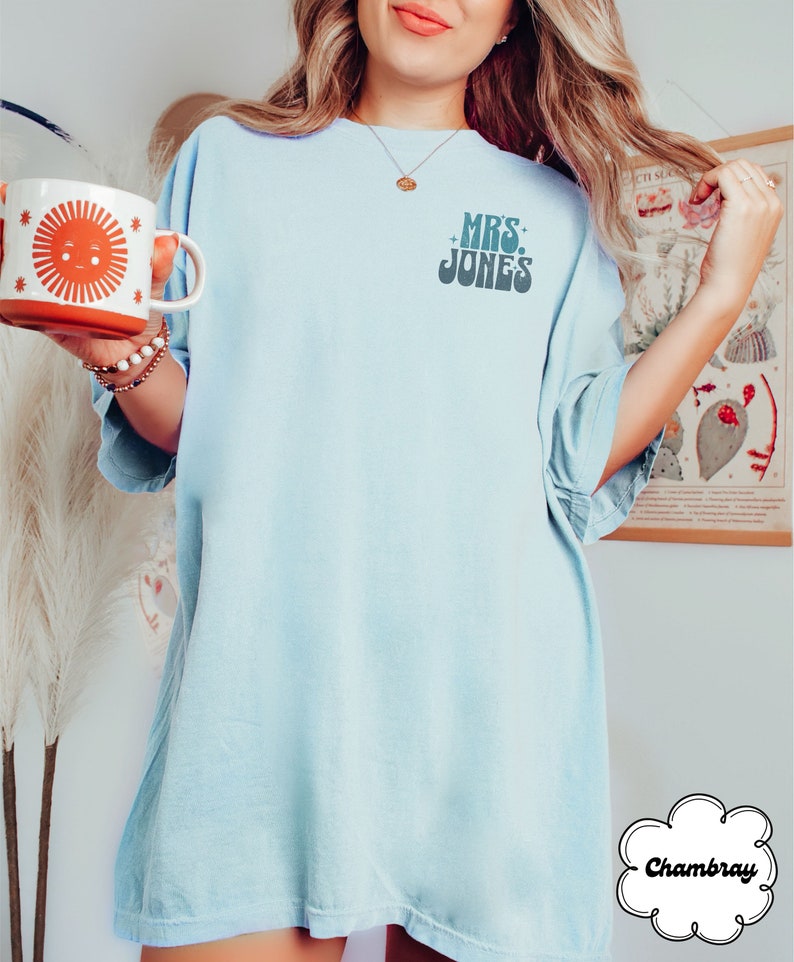 Może przedstawiać: Jasno błękitny, oversize'owy t-shirt z napisem "MRS. JONES" w retro czcionce. Koszulka wykonana jest z miękkiej, wygodnej tkaniny chambray.