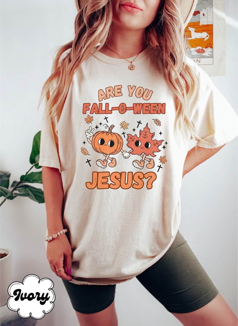 May include: A white t-shirt with the text "Are you Fall-O-Ween Jesus?" in orange and brown lettering. The text is accompanied by a cartoon pumpkin and leaf holding hands.
