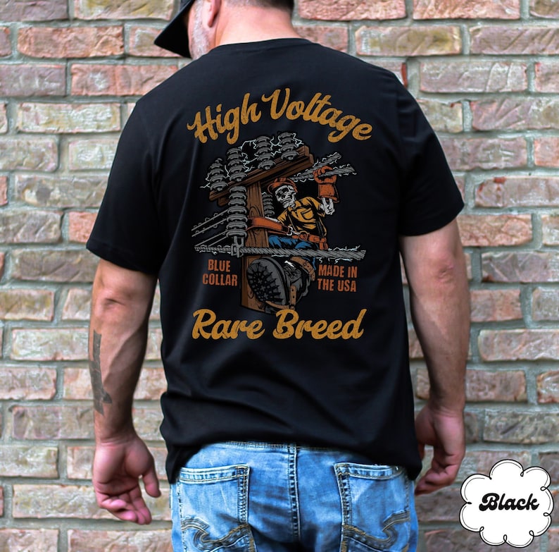 May include: Black t-shirt with a graphic of a skeleton working on a high voltage power line. The text "High Voltage", "Blue Collar", "Made in the USA", and "Rare Breed" is printed on the shirt.