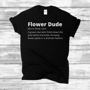 May include: Black t-shirt with white text that reads "Flower Dude (flou-er Dood) noun A grown man who frolics down the aisle before the bride, throwing flower petals in a dramatic fashion."