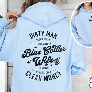 Puede incluir: Sudadera con capucha azul claro con un estampado gr&aacute;fico negro que dice "Dirty Man Blue Collar Rare Breed Blue Collar Wife Est. MMXVIII Dollar Club Clean Money".
