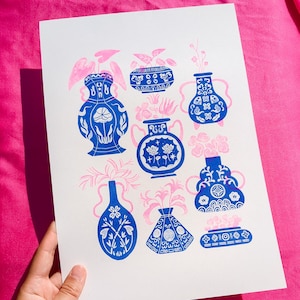 Könnte beinhalten: Ein weißer Hintergrund mit einem blauen und weißen Blumenmuster. Das Muster zeigt verschiedene blaue und weiße Vasen mit Blumendesigns. Die Vasen sind symmetrisch angeordnet.