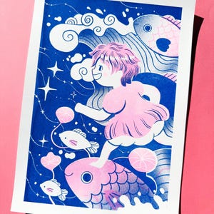 May include: A whimsical art print featuring a young person with pink hair and a pink dress, riding a large pink fish through a blue ocean. The illustration includes white clouds, stars, and smaller fish, creating a dreamlike scene.