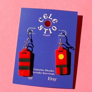 Può includere: Orecchini rettangolari rossi in acrilico con strisce nere e un cerchio giallo. Gli orecchini hanno ganci argentati e sono esposti su una carta blu con il testo "Celestio Studio Acrylic Earrings Etsy".