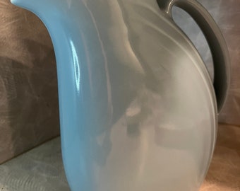 May include: A light blue ceramic pitcher with a rounded body and a handle. The pitcher has a smooth, glossy finish.