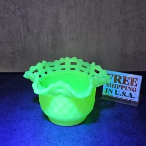 May include: A vibrant neon green glass bowl featuring a ruffled, lattice-style rim and a textured hobnail pattern on the exterior. The bowl glows under ultraviolet light, and a small sign nearby displays the text FREE SHIPPING IN U.S.A.