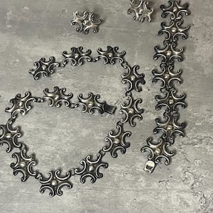 Peut inclure: Un ensemble de collier, bracelet et boucles d'oreilles en argent avec un motif g&eacute;om&eacute;trique. Les bijoux sont faits de maillons en argent entrelac&eacute;s avec un cercle central sur&eacute;lev&eacute; sur chaque maillon.
