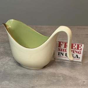 Peut inclure: Saucière crème avec un intérieur vert clair et un bord doré. La saucière a une poignée incurvée et un bec verseur. Le texte "FREE SHIPPING IN U.S.A." est visible en arrière-plan.