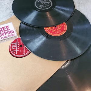 May include: Three black vinyl records stacked on top of a brown paper bag. The top record has a white label with the text "Capitol" and "Divorce Me C & P" in black. The middle record has a red label with the text "King of the 1319-A" and "Allons A Lafayette" in white. The bottom record is black with no visible label. A red and white label with the text "4 Star" is visible on the bag.