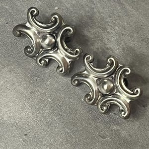 Peut inclure: Une paire de boucles d'oreilles en argent avec un design orn&eacute; et tourbillonnant. Les boucles d'oreilles ont un centre rond et sur&eacute;lev&eacute;.