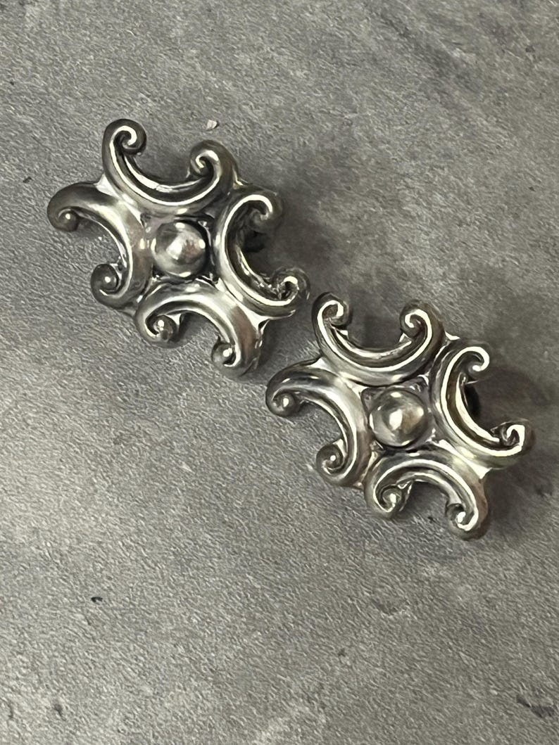 Peut inclure: Une paire de boucles d'oreilles en argent avec un design orn&eacute; et tourbillonnant. Les boucles d'oreilles ont un centre rond et sur&eacute;lev&eacute;.