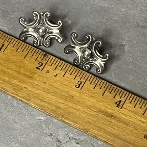Peut inclure: Une paire de boucles d'oreilles en argent avec un motif d&eacute;coratif. Les boucles d'oreilles mesurent environ 2,5 cm de diam&egrave;tre et ont une petite perle au centre.