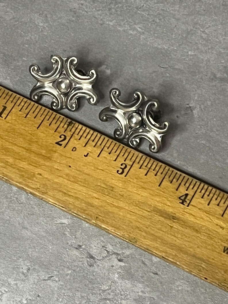 Peut inclure: Une paire de boucles d'oreilles en argent avec un motif d&eacute;coratif. Les boucles d'oreilles mesurent environ 2,5 cm de diam&egrave;tre et ont une petite perle au centre.