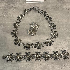 Peut inclure: Un ensemble de bijoux en argent compos&eacute; d'un collier, d'un bracelet et de boucles d'oreilles. Les bijoux sont en argent sterling et pr&eacute;sentent un motif r&eacute;p&eacute;titif de petites formes arrondies.