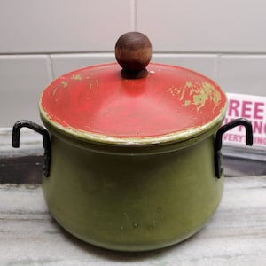 May include: Green enamel pot with a red lid and a wooden knob. The pot has two black metal handles.