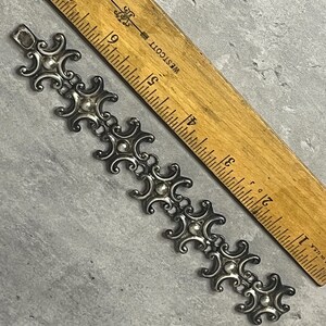 Peut inclure: Un bracelet en argent avec un motif r&eacute;p&eacute;t&eacute; de croissants de lune stylis&eacute;s et de petites perles rondes. Le bracelet mesure environ 15 cm de long et est mesur&eacute; contre une r&egrave;gle en bois.