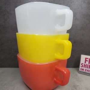 May include: Three stacked square mugs with handles. The top mug is white, the middle mug is yellow, and the bottom mug is orange.