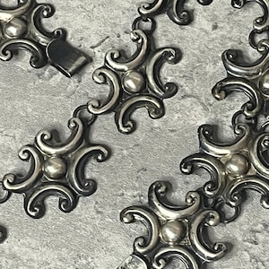 Peut inclure: Un collier en argent avec un design orn&eacute; et d&eacute;taill&eacute;. Chaque maillon pr&eacute;sente une forme circulaire stylis&eacute;e avec une perle centrale en relief. La cha&icirc;ne est compos&eacute;e de maillons entrelac&eacute;s, cr&eacute;ant un motif continu.